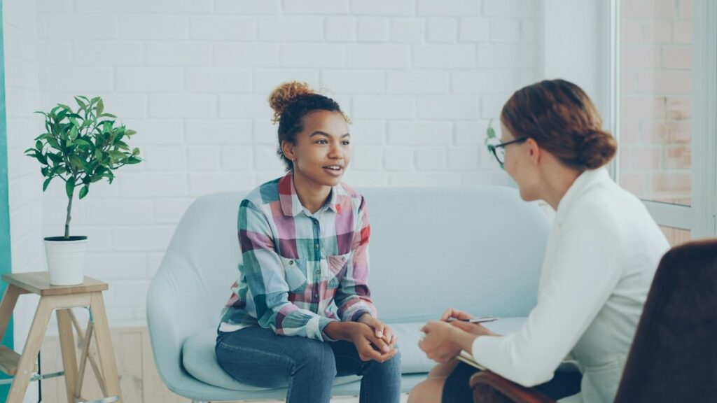 A counselor listens as an adult discusses grief in a quiet office with tissues and a notebook nearby.