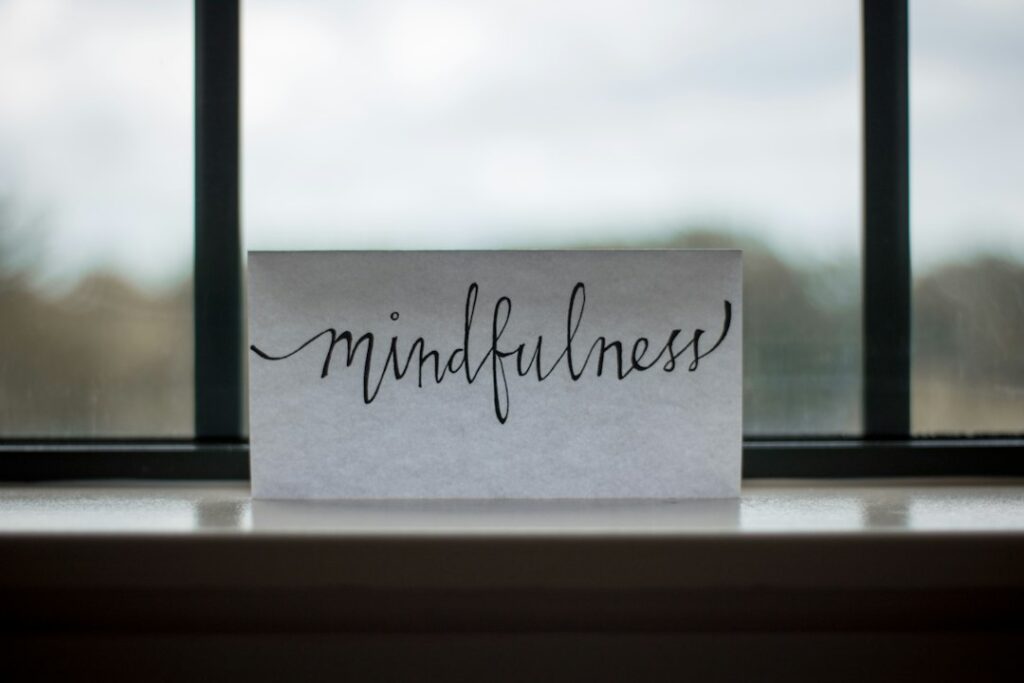 Adult sitting quietly by a window, practicing mindful breathing with both feet grounded on the floor.