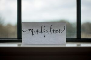 Adult sitting quietly by a window, practicing mindful breathing with both feet grounded on the floor.