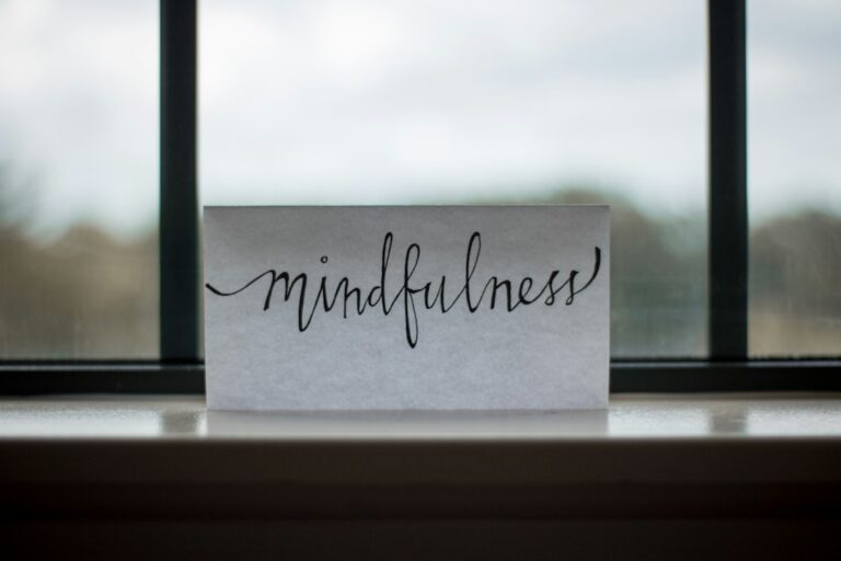 Adult sitting quietly by a window, practicing mindful breathing with both feet grounded on the floor.